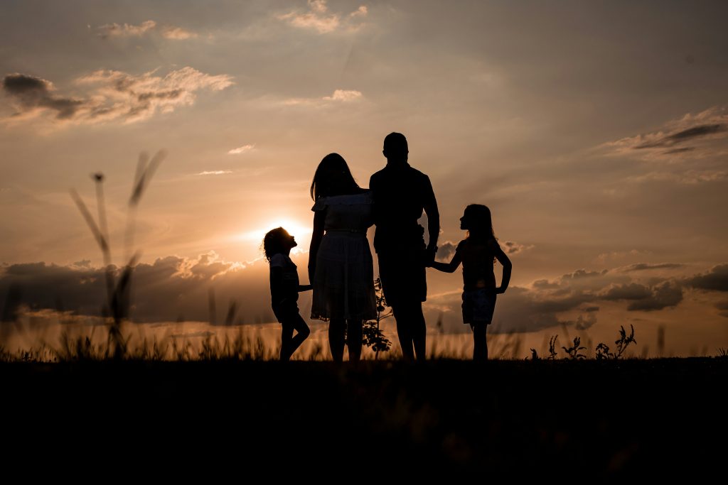 Silhouette of two parents standing with their two children outdoors at sunset.